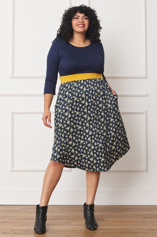 A woman with curly hair smiles, adorning a Plus Curved Hem Band Midi Dress made from a polyester and spandex blend. The black dress showcases three-quarter sleeves and is accented with a red waistband. The skirt is decorated with an eye-catching floral pattern of large pink and orange flowers.