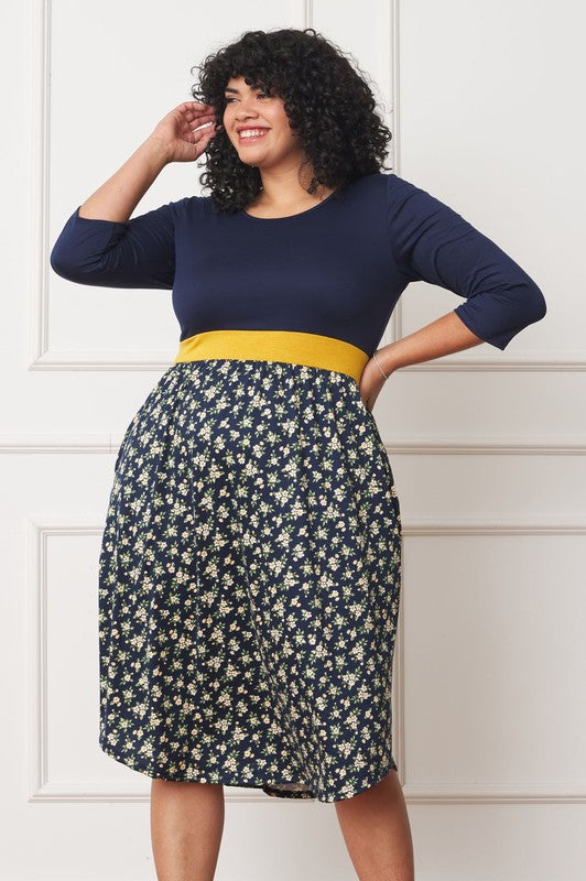 A woman with curly hair smiles, adorning a Plus Curved Hem Band Midi Dress made from a polyester and spandex blend. The black dress showcases three-quarter sleeves and is accented with a red waistband. The skirt is decorated with an eye-catching floral pattern of large pink and orange flowers.