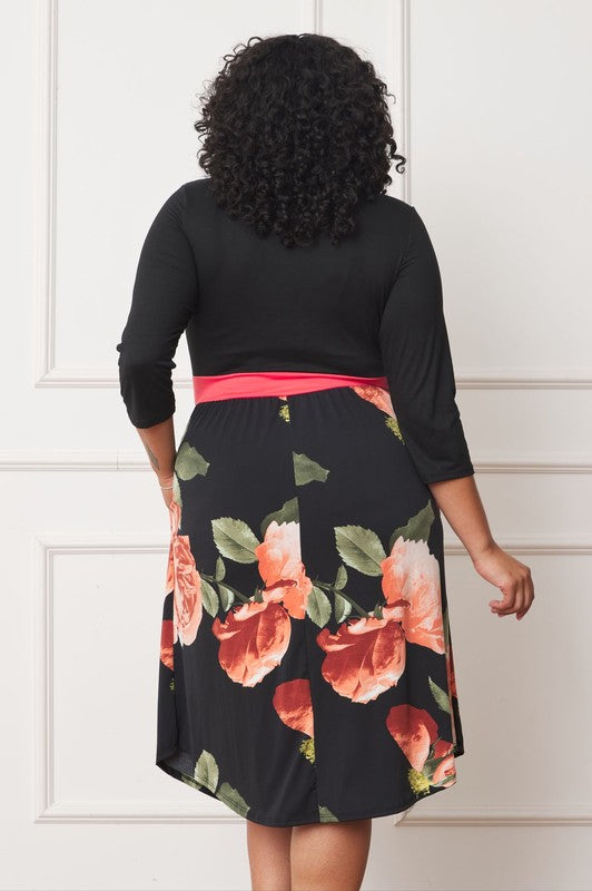 A woman with curly hair smiles, adorning a Plus Curved Hem Band Midi Dress made from a polyester and spandex blend. The black dress showcases three-quarter sleeves and is accented with a red waistband. The skirt is decorated with an eye-catching floral pattern of large pink and orange flowers.