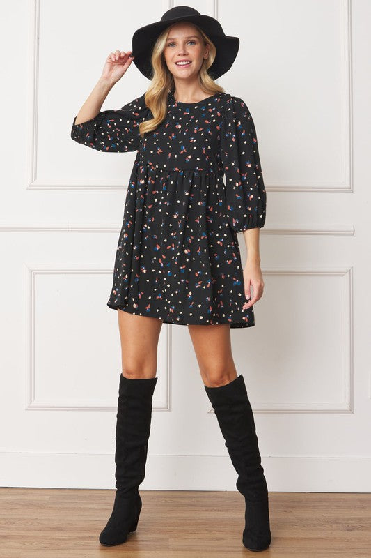 A woman stands indoors wearing the Abstract Polka Dot Bishop Sleeve Mini Dress, black knee-high boots, and a black floppy hat. She is smiling and looking slightly to the side in her stylish mini dress with a colorful pattern.