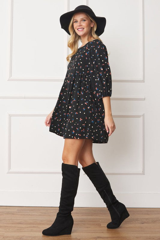A woman stands indoors wearing the Abstract Polka Dot Bishop Sleeve Mini Dress, black knee-high boots, and a black floppy hat. She is smiling and looking slightly to the side in her stylish mini dress with a colorful pattern.