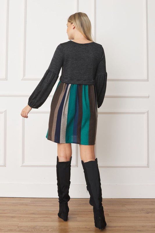 A woman with curly hair, dressed in a Plus Balloon Sleeve Pullover Dress featuring a gray top and vertical stripes in various colors on the high-waisted skirt, stands against a plain background. Her attire includes elements of Polyester Spandex for comfort and style.