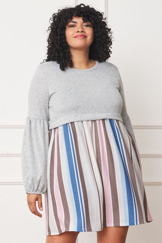 A woman with curly hair, dressed in a Plus Balloon Sleeve Pullover Dress featuring a gray top and vertical stripes in various colors on the high-waisted skirt, stands against a plain background. Her attire includes elements of Polyester Spandex for comfort and style.