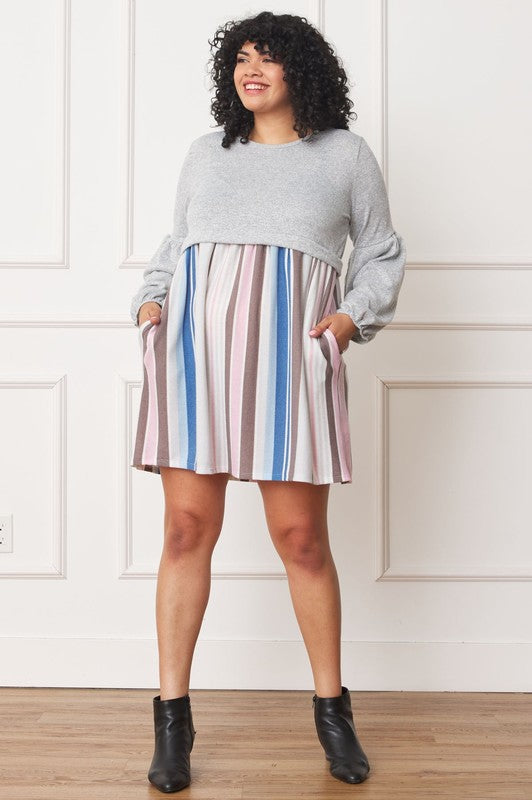 A woman with curly hair, dressed in a Plus Balloon Sleeve Pullover Dress featuring a gray top and vertical stripes in various colors on the high-waisted skirt, stands against a plain background. Her attire includes elements of Polyester Spandex for comfort and style.
