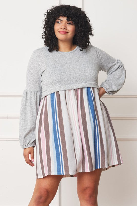 A woman with curly hair, dressed in a Plus Balloon Sleeve Pullover Dress featuring a gray top and vertical stripes in various colors on the high-waisted skirt, stands against a plain background. Her attire includes elements of Polyester Spandex for comfort and style.