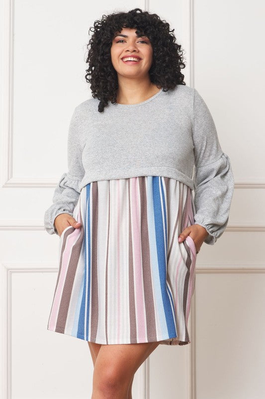 A woman with curly hair, dressed in a Plus Balloon Sleeve Pullover Dress featuring a gray top and vertical stripes in various colors on the high-waisted skirt, stands against a plain background. Her attire includes elements of Polyester Spandex for comfort and style.