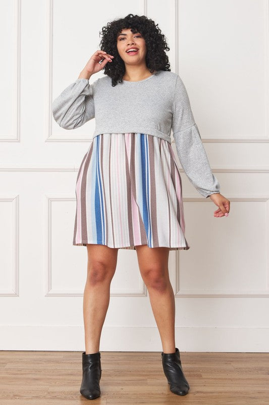A woman with curly hair, dressed in a Plus Balloon Sleeve Pullover Dress featuring a gray top and vertical stripes in various colors on the high-waisted skirt, stands against a plain background. Her attire includes elements of Polyester Spandex for comfort and style.