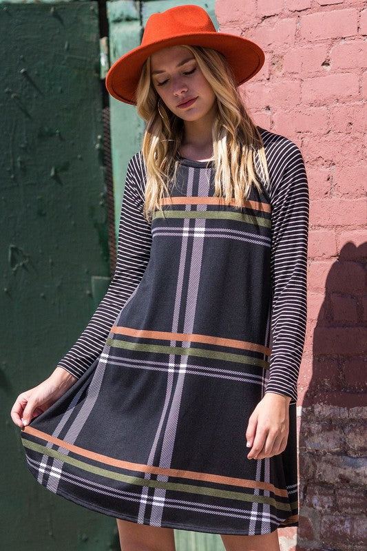 A person stands against a brick wall in a Stripe Sleeve A-Line Mini Dress with black and orange plaid, paired with an orange hat, smiling.