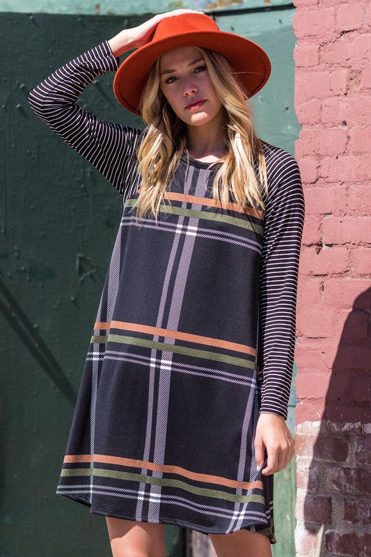 A person stands against a brick wall in a Stripe Sleeve A-Line Mini Dress with black and orange plaid, paired with an orange hat, smiling.
