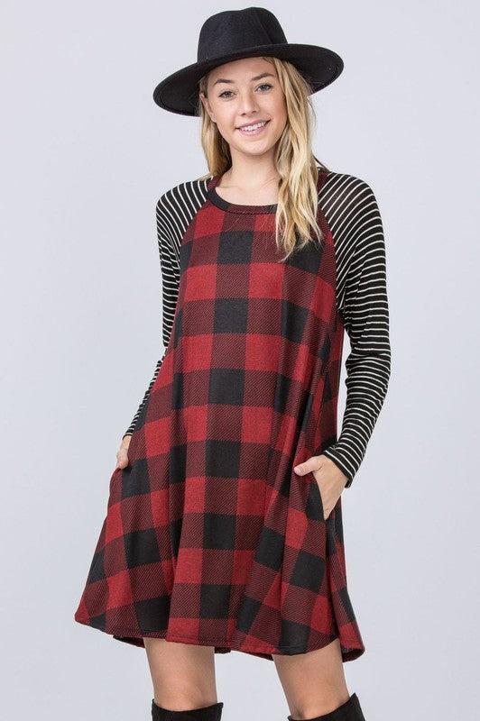 A person stands against a brick wall in a Stripe Sleeve A-Line Mini Dress with black and orange plaid, paired with an orange hat, smiling.