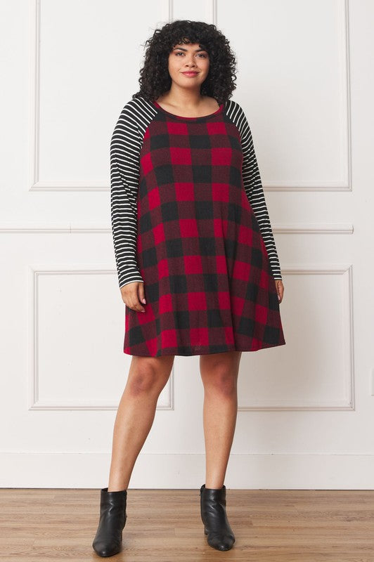 A person stands wearing the Plus Stripe Sleeve A-Line Mini Dress with red and black plaid pattern and black and white stripe sleeves, smiling slightly.