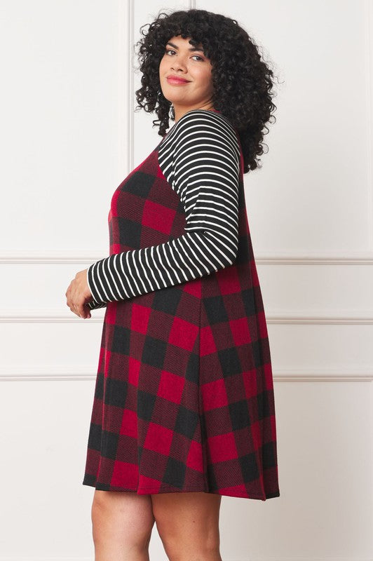 A person stands wearing the Plus Stripe Sleeve A-Line Mini Dress with red and black plaid pattern and black and white stripe sleeves, smiling slightly.