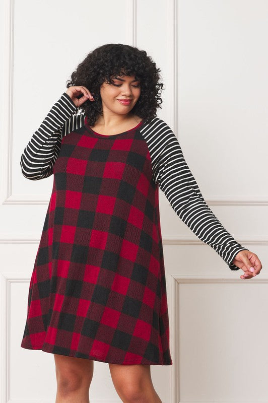 A person stands wearing the Plus Stripe Sleeve A-Line Mini Dress with red and black plaid pattern and black and white stripe sleeves, smiling slightly.