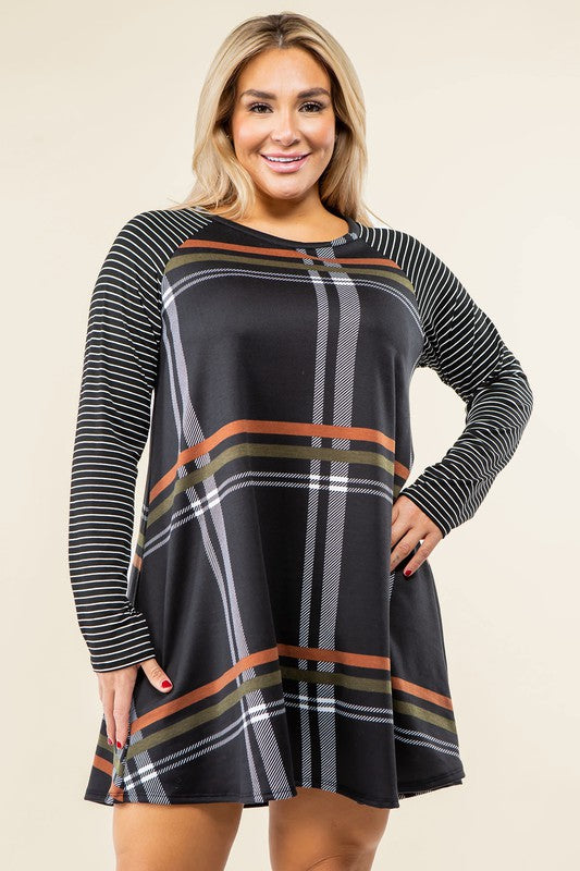 A person stands wearing the Plus Stripe Sleeve A-Line Mini Dress with red and black plaid pattern and black and white stripe sleeves, smiling slightly.