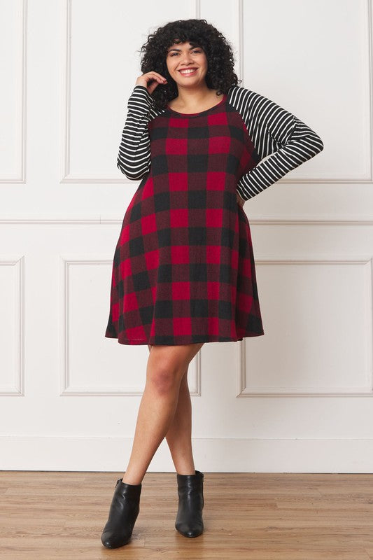 A person stands wearing the Plus Stripe Sleeve A-Line Mini Dress with red and black plaid pattern and black and white stripe sleeves, smiling slightly.