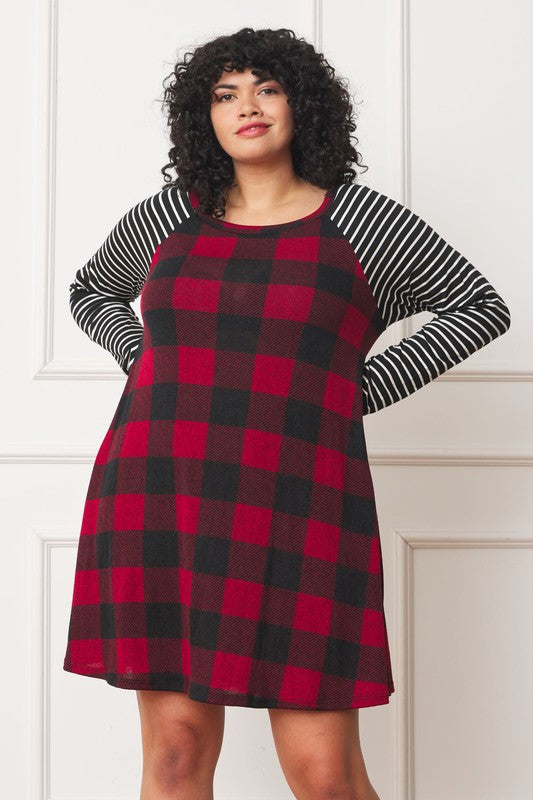 A person stands wearing the Plus Stripe Sleeve A-Line Mini Dress with red and black plaid pattern and black and white stripe sleeves, smiling slightly.