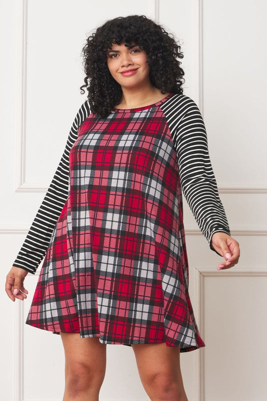 A woman with curly hair is standing in front of a white paneled wall, wearing a red, black, and white plaid Plus Stripe Sleeve A-Line Mini Dress. The dress features black and white striped polyester sleeves.