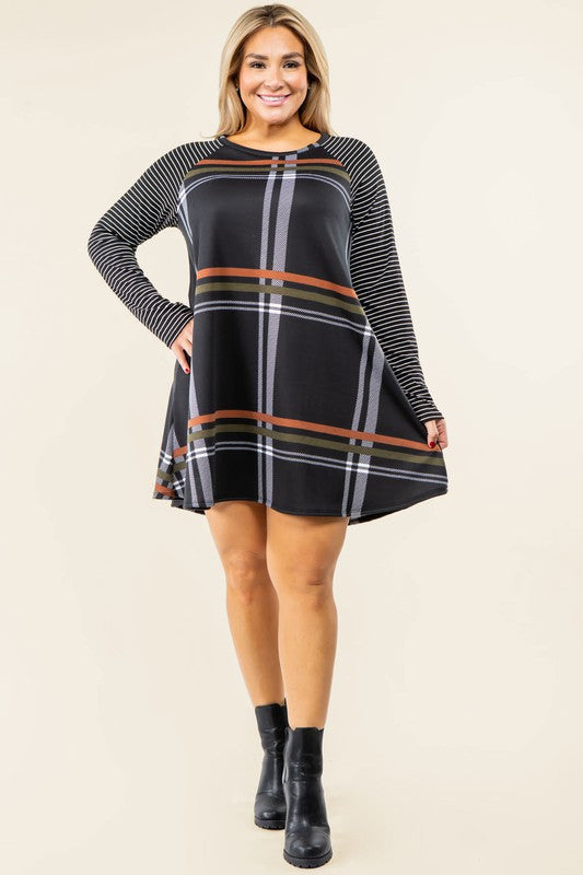 A person stands wearing the Plus Stripe Sleeve A-Line Mini Dress with red and black plaid pattern and black and white stripe sleeves, smiling slightly.