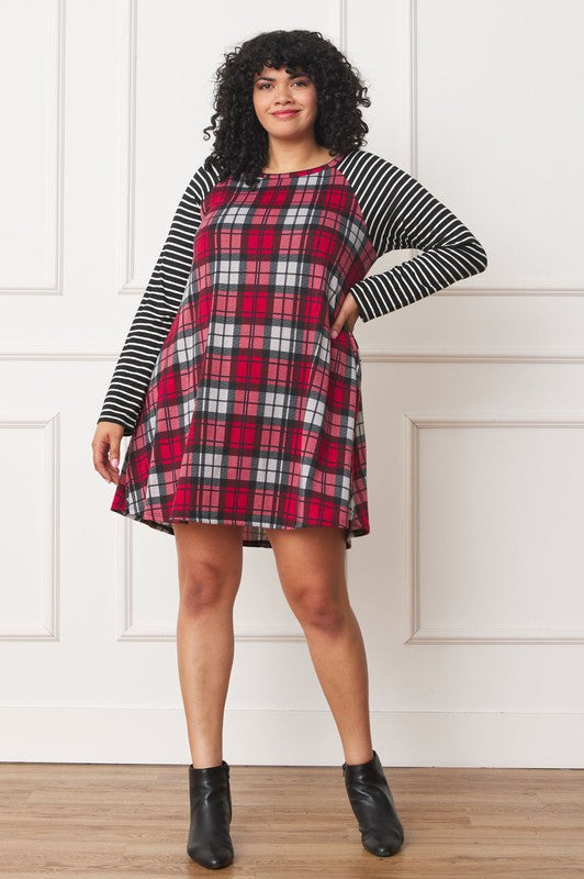 A person stands wearing the Plus Stripe Sleeve A-Line Mini Dress with red and black plaid pattern and black and white stripe sleeves, smiling slightly.