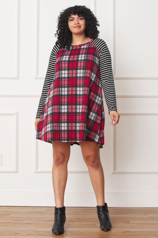 A person stands wearing the Plus Stripe Sleeve A-Line Mini Dress with red and black plaid pattern and black and white stripe sleeves, smiling slightly.