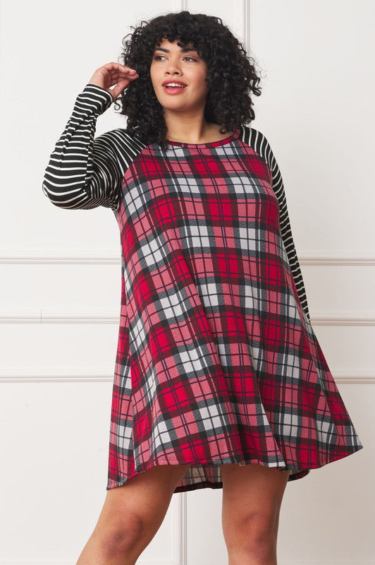 A person stands wearing the Plus Stripe Sleeve A-Line Mini Dress with red and black plaid pattern and black and white stripe sleeves, smiling slightly.