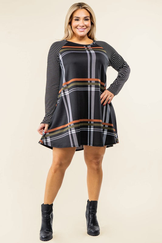 A person stands wearing the Plus Stripe Sleeve A-Line Mini Dress with red and black plaid pattern and black and white stripe sleeves, smiling slightly.