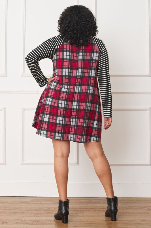 A person stands wearing the Plus Stripe Sleeve A-Line Mini Dress with red and black plaid pattern and black and white stripe sleeves, smiling slightly.