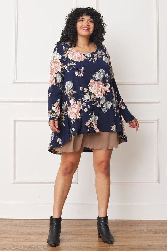 A person with curly hair smiles while wearing a Floral Chiffon Layered Mini Dress with long sleeves and a high-low hemline, standing against a neutral background.