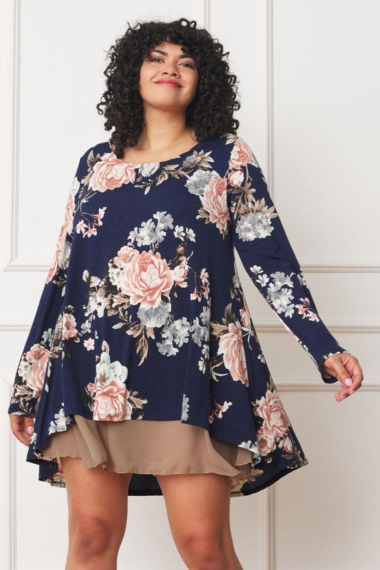 A person with curly hair smiles while wearing a Floral Chiffon Layered Mini Dress with long sleeves and a high-low hemline, standing against a neutral background.