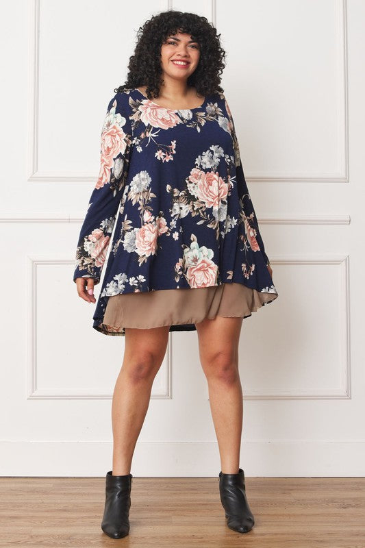 A person with curly hair smiles while wearing a Floral Chiffon Layered Mini Dress with long sleeves and a high-low hemline, standing against a neutral background.
