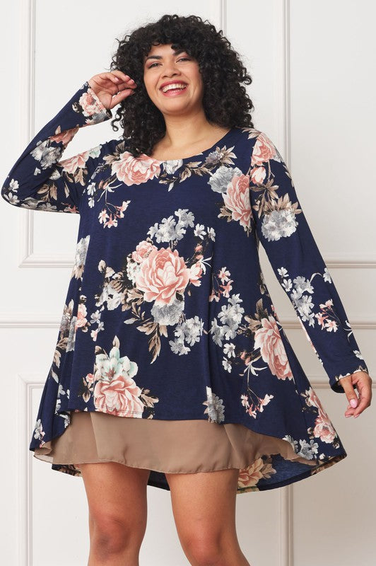 A person with curly hair smiles while wearing a Floral Chiffon Layered Mini Dress with long sleeves and a high-low hemline, standing against a neutral background.
