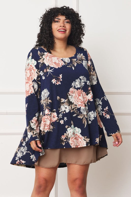 A person with curly hair smiles while wearing a Floral Chiffon Layered Mini Dress with long sleeves and a high-low hemline, standing against a neutral background.