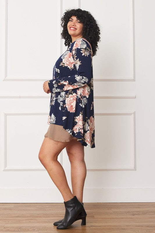 A person with curly hair smiles while wearing a Floral Chiffon Layered Mini Dress with long sleeves and a high-low hemline, standing against a neutral background.