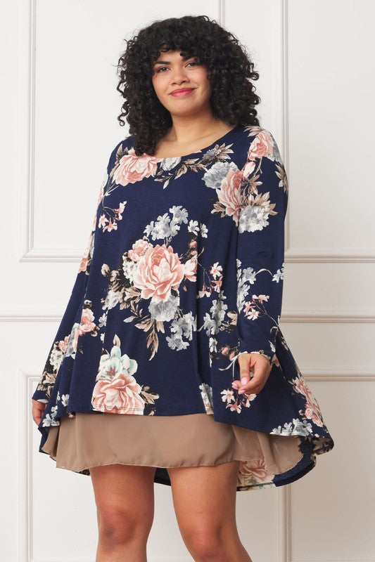 A person with curly hair smiles while wearing a Floral Chiffon Layered Mini Dress with long sleeves and a high-low hemline, standing against a neutral background.