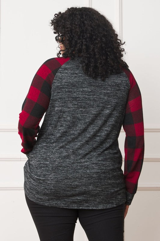 A woman with curly hair, wearing a Plus Checker Sleeve Sequin Pocket Tunic featuring dark grey fabric and red plaid checker sleeves, stands against a white background. Made in the United States, she has her hand in her pocket and is smiling.
