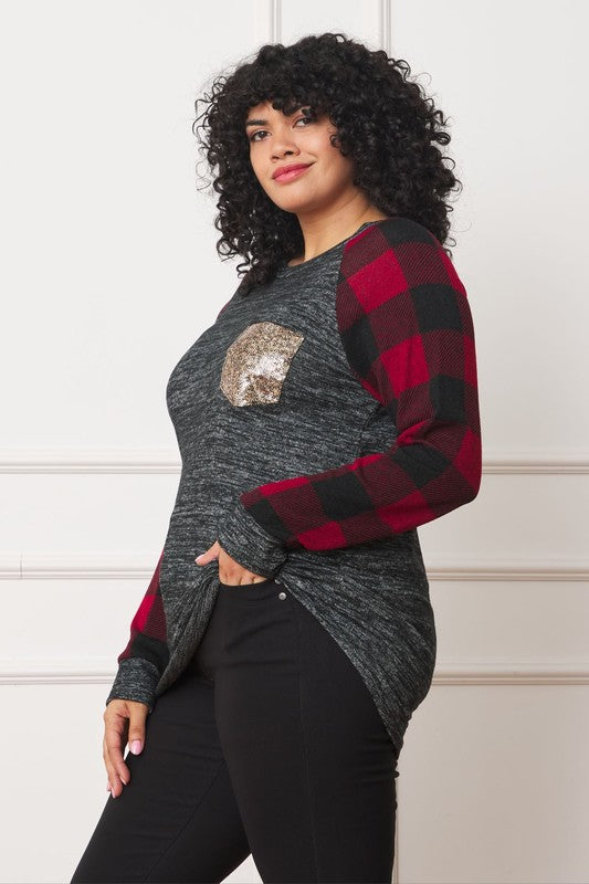 A woman with curly hair, wearing a Plus Checker Sleeve Sequin Pocket Tunic featuring dark grey fabric and red plaid checker sleeves, stands against a white background. Made in the United States, she has her hand in her pocket and is smiling.