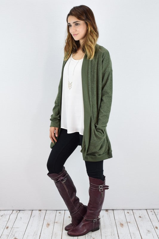 Person wearing a Plus Solid Drape Pocket Cardigan in green over a white shirt and black pants, standing in front of a white wall.