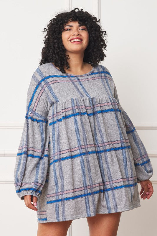A person with curly hair wearing a Plus Plaid Empire Waist Balloon Sleeve Mini Dress stands against a white wall, smiling.
