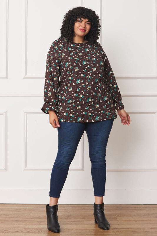 A person wearing the Plus Floral Ruffle Sleeve Tunic made from 100% polyester and blue jeans stands against a white wall.