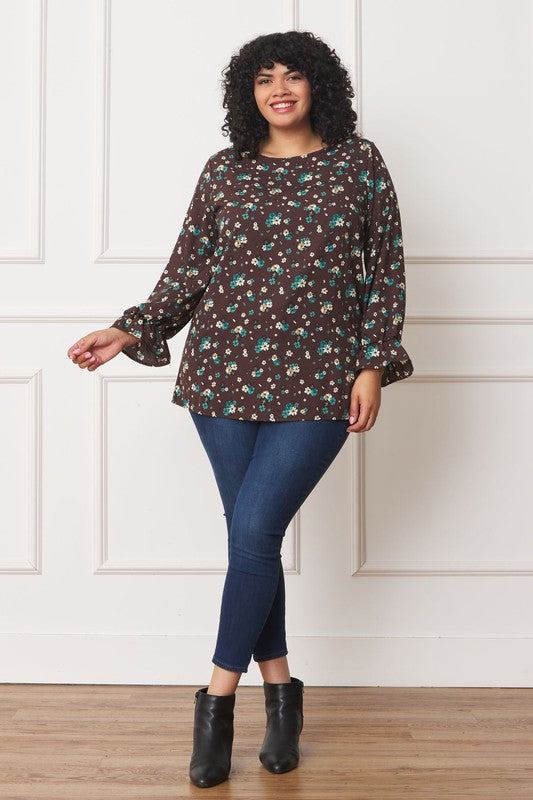 A person wearing the Plus Floral Ruffle Sleeve Tunic made from 100% polyester and blue jeans stands against a white wall.