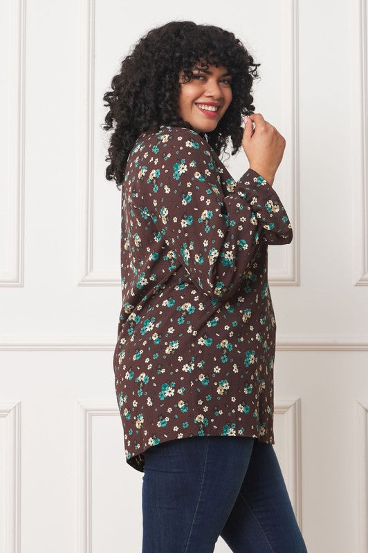A person wearing the Plus Floral Ruffle Sleeve Tunic made from 100% polyester and blue jeans stands against a white wall.