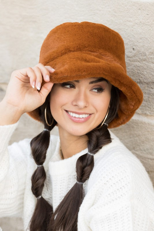 A woman in a white sweater smiling and tipping her Plush Bucket Hat.