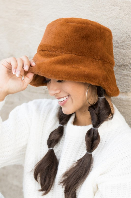 A woman in a white sweater smiling and tipping her Plush Bucket Hat.
