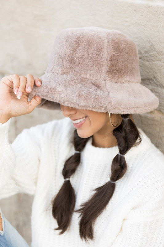 A woman in a white sweater smiling and tipping her Plush Bucket Hat.