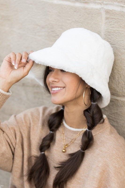 A woman in a white sweater smiling and tipping her Plush Bucket Hat.