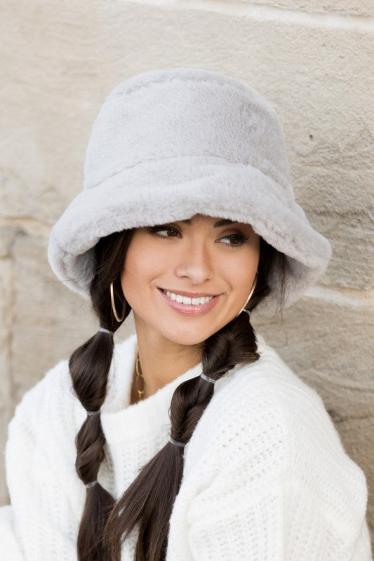 A woman in a white sweater smiling and tipping her Plush Bucket Hat.