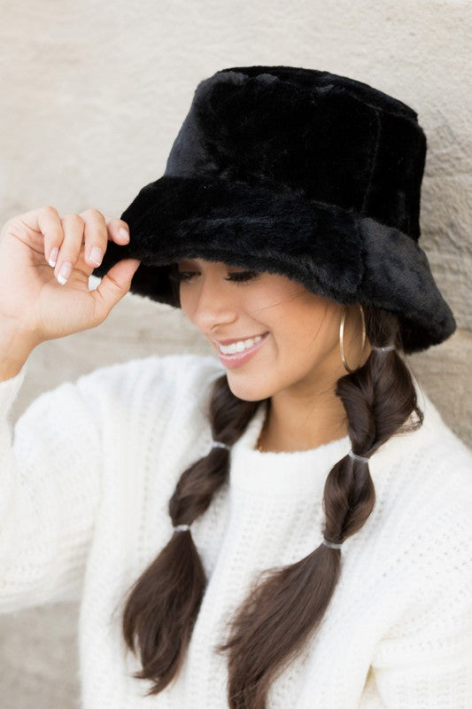 A woman in a white sweater smiling and tipping her Plush Bucket Hat.