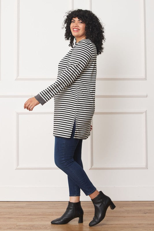 A person with curly hair smiles while wearing the Plus Stripe V-Stich Tunic, a black-and-white striped shirt designed in plus size, standing against a plain background.