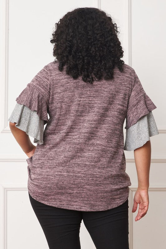 A woman stands against a plain background, wearing a Color Block Sleeve Ruffle Knit Top made of polyester and spandex, paired with light blue jeans. She has long dark hair and is looking towards the camera.