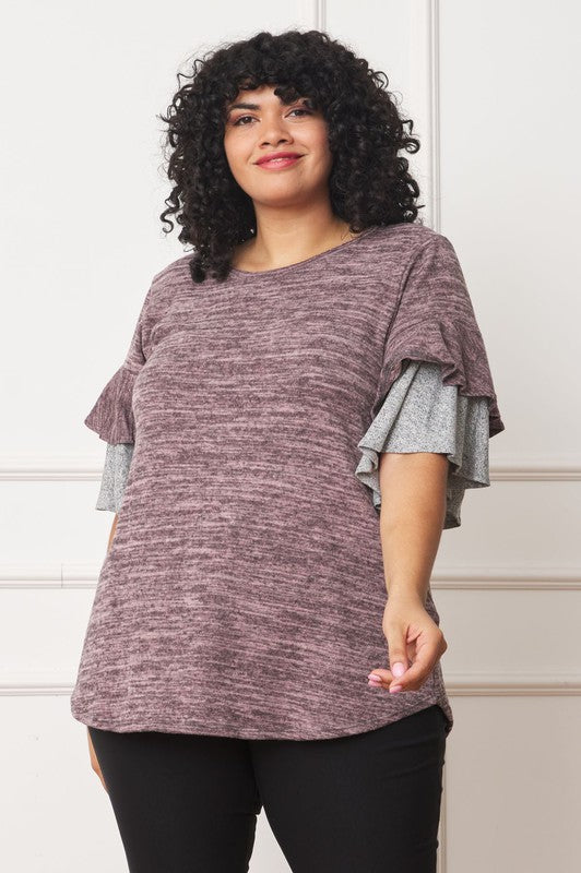 A woman stands against a plain background, wearing a Color Block Sleeve Ruffle Knit Top made of polyester and spandex, paired with light blue jeans. She has long dark hair and is looking towards the camera.